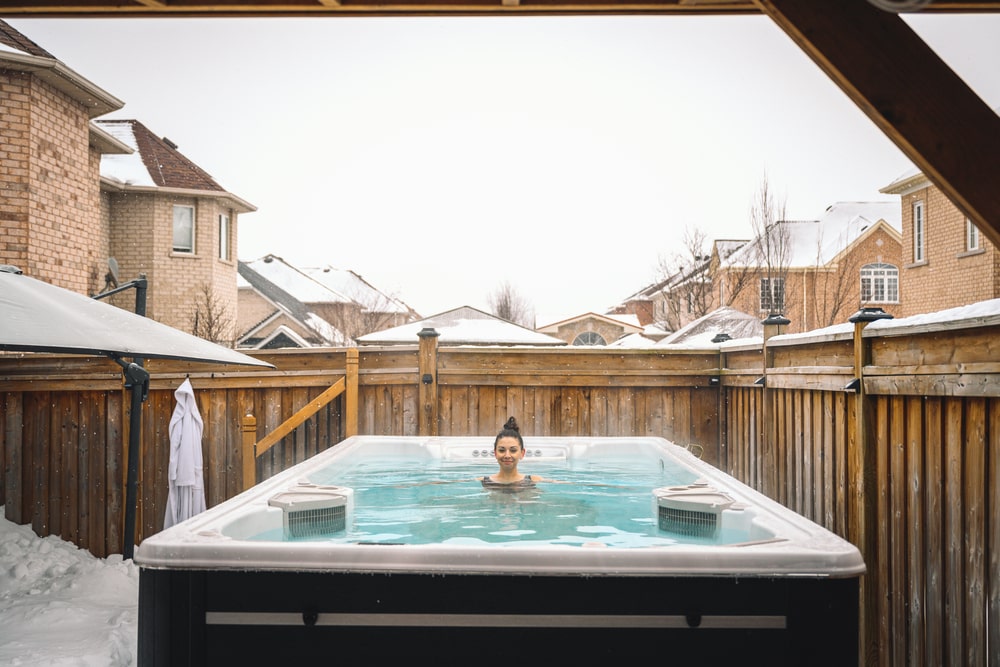 woman in a wooden swim spa in a snowy backyard with houses