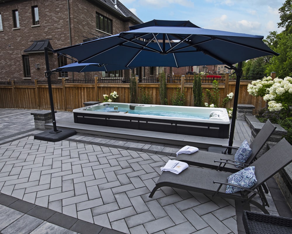 modern swim spa, comfortable lounging chairs with decorative cushions, a large blue umbrella