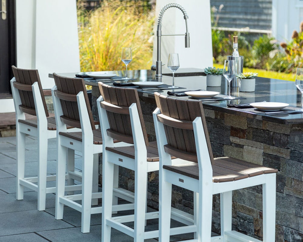Outdoor dining setup with modern white and brown chairs, stone countertop, tableware, and wine bottle in a garden setting